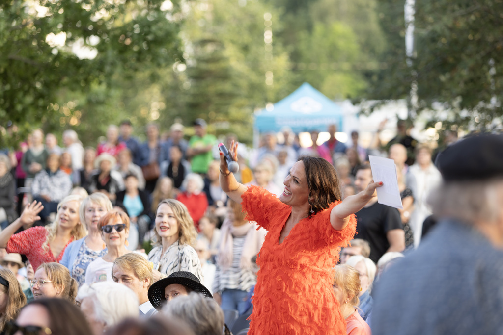 Johanna Hautasaari juontaa ja laulattaa yleisöä yhteislaulutapahtumassa